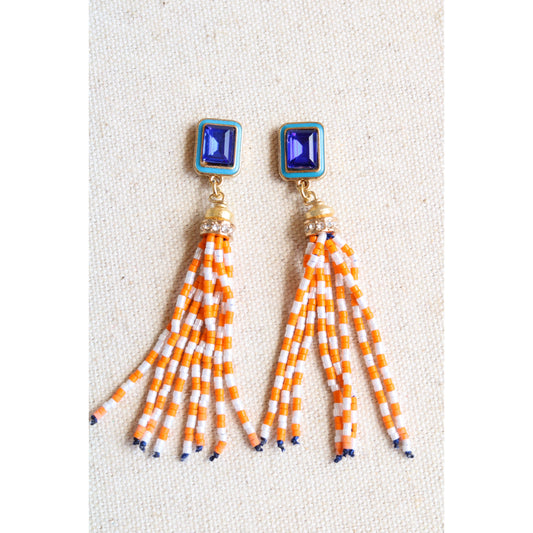 Pair of earrings with blue tops and orange and white striped fringes on a light background