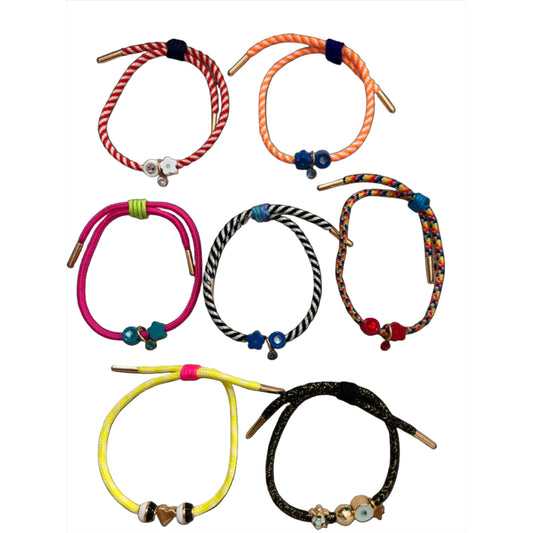 Seven cord bracelets with brass tips are laid out in a line to show color and charm variety