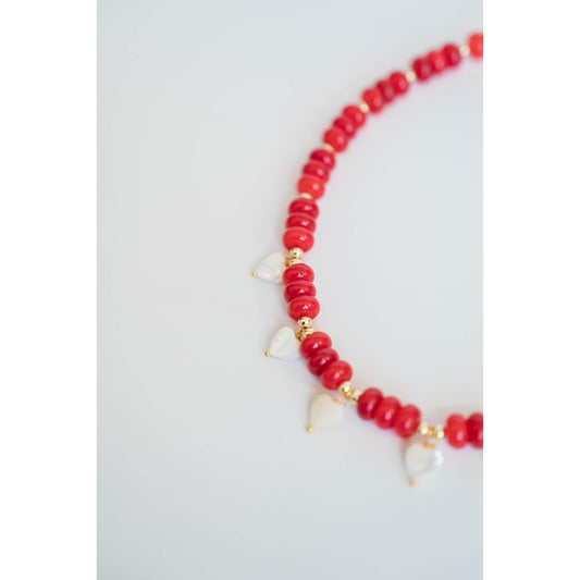 necklace with red beads, gold spacers, and white pearl heart charms on a light background