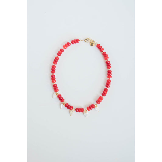 Necklace with red beads, gold spacers, white pearl heart charms and a gold pave clasp on a light gray background