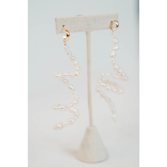 flexible pearl drop earrings with gold huggie posts on a neutral earring stand against a light gray background