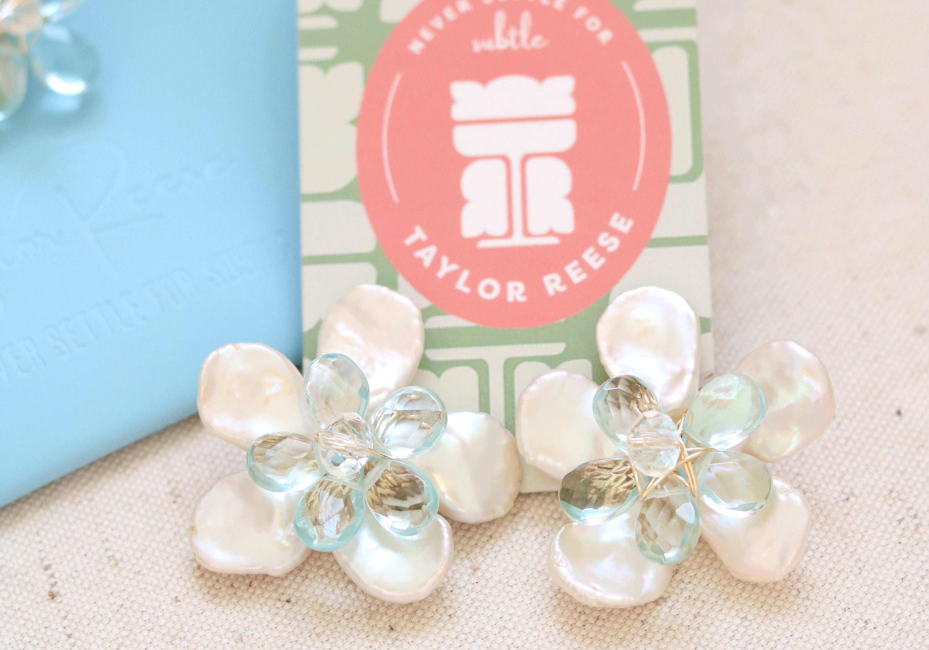 Handcrafted custom bridal earrings made in North Carolina featuring mother of pearl petals and blue quartz stones, designed for a beach wedding.