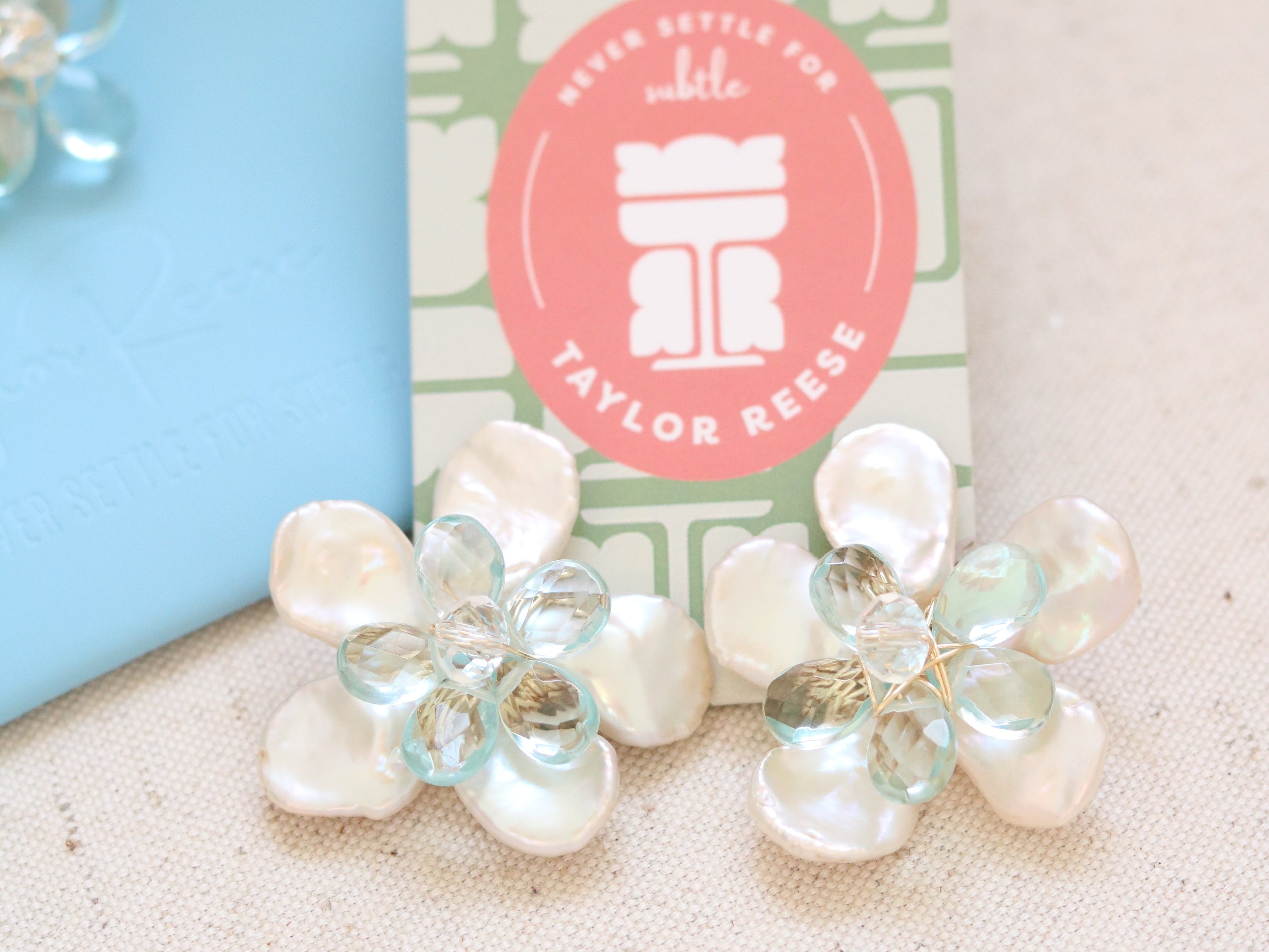 Handcrafted custom bridal earrings made in North Carolina featuring mother of pearl petals and blue quartz stones, designed for a beach wedding.