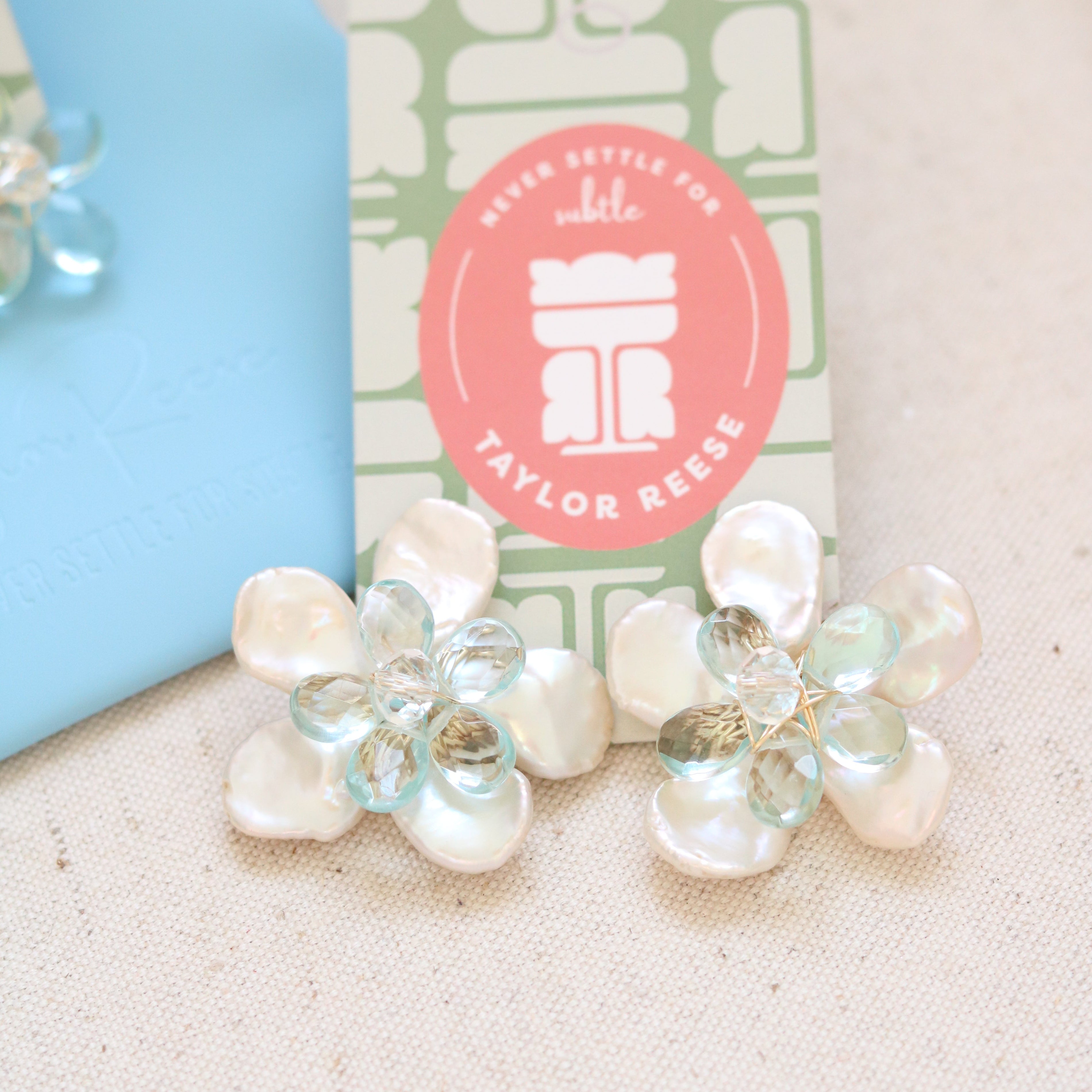 Handcrafted custom bridal earrings made in North Carolina featuring mother of pearl petals and blue quartz stones, designed for a beach wedding.