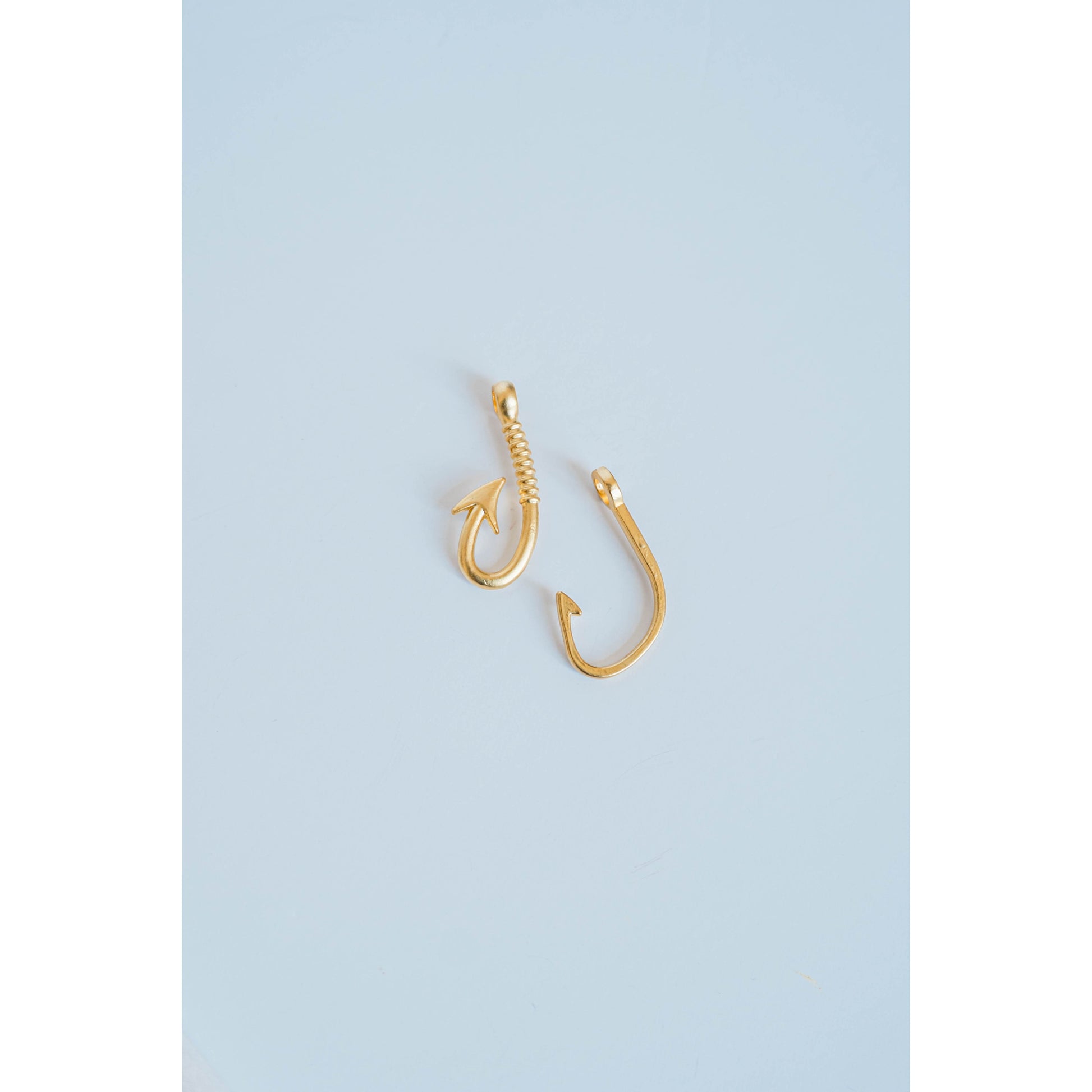 two gold fishing hook charms on a light grey background