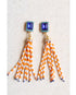 Pair of earrings with blue tops and orange and white striped fringes on a light background
