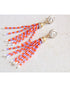Beaded orange and purple tassel earrings on a beige fabric background
