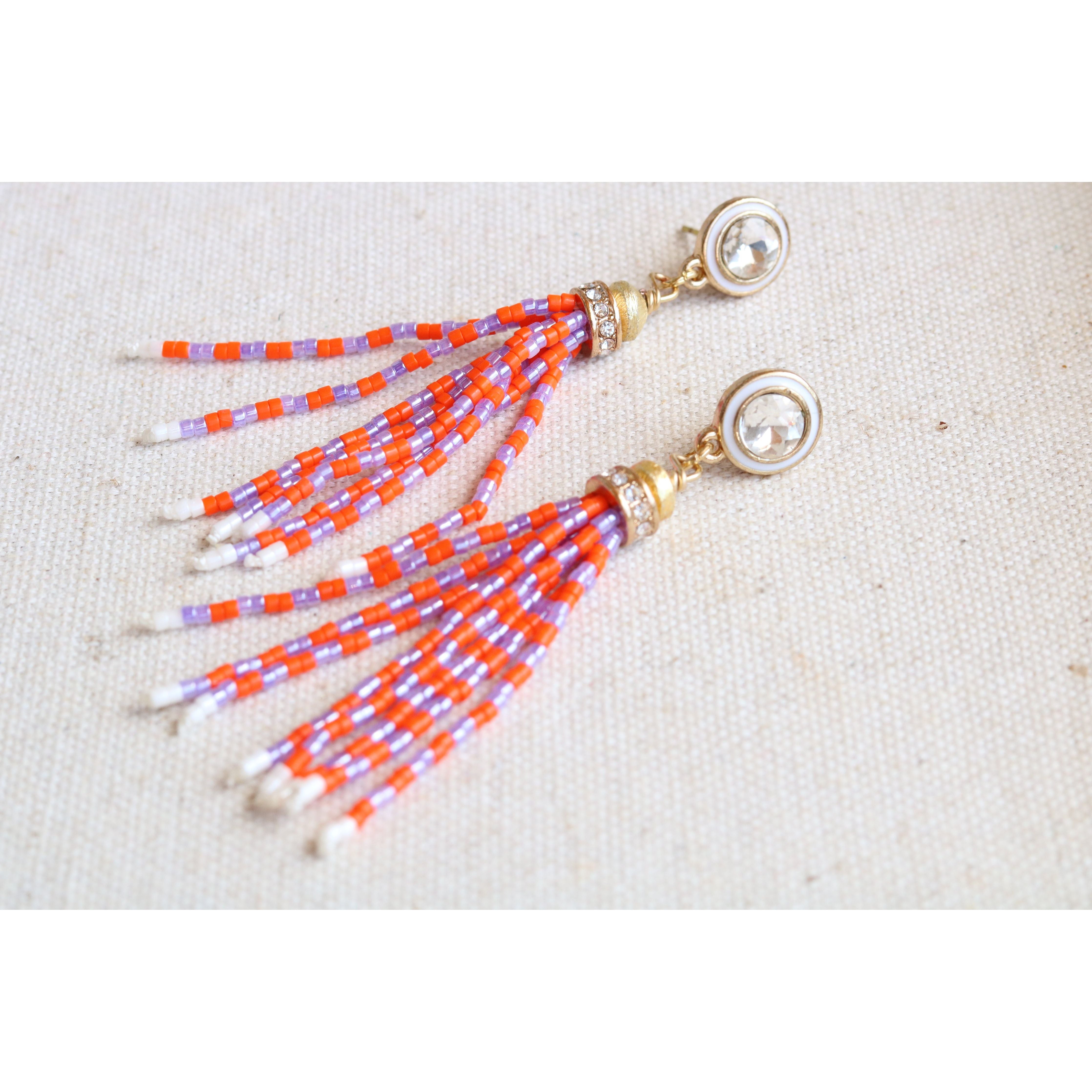 Beaded orange and purple tassel earrings on a beige fabric background