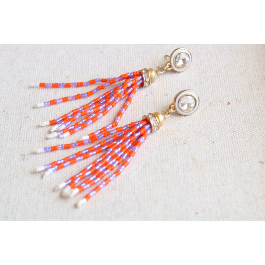 Beaded orange and purple tassel earrings on a beige fabric background
