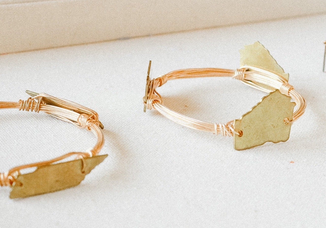 Gold hoop earrings with leaf-shaped charms on a white surface.