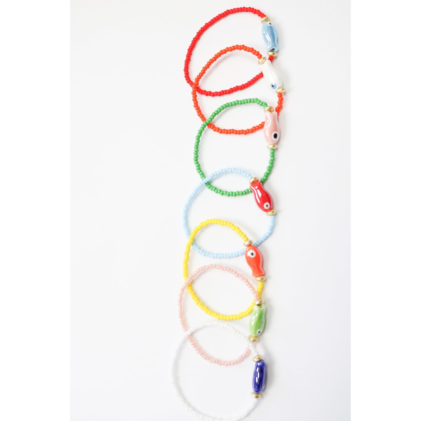 An assortment of colorful bracelets in a line. The image shows a single painted ceramic fish bead on a colored glass bead bracelet.