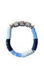 A beaded stretch bracelet with alternating light blue, navy blue, and white disc beads, accented by four silver-toned charm beads at the top, displayed on a wooden surface.
