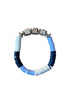 A beaded stretch bracelet with alternating light blue, navy blue, and white disc beads, accented by four silver-toned charm beads at the top, displayed on a wooden surface.