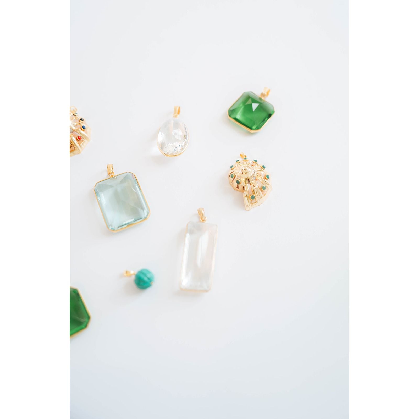 collection of various crystal pendants with gold frames in green, aquamarine, glass, and turquoise against a light background