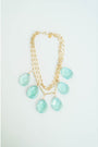 Gold layered chain necklace with aqua colored teardrop pendants on a light grey background