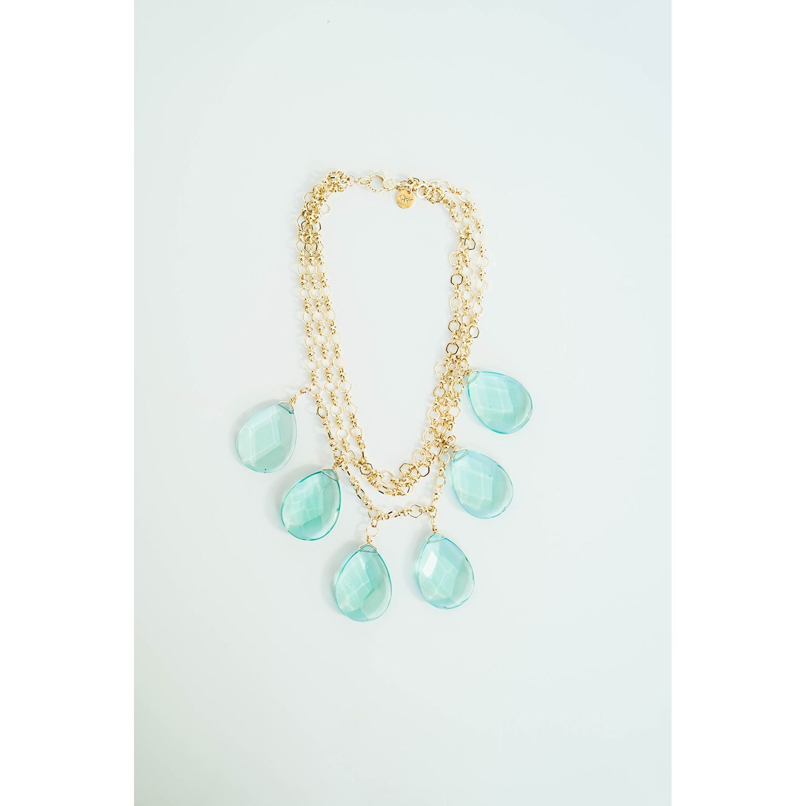 Gold layered chain necklace with aqua colored teardrop pendants on a light grey background