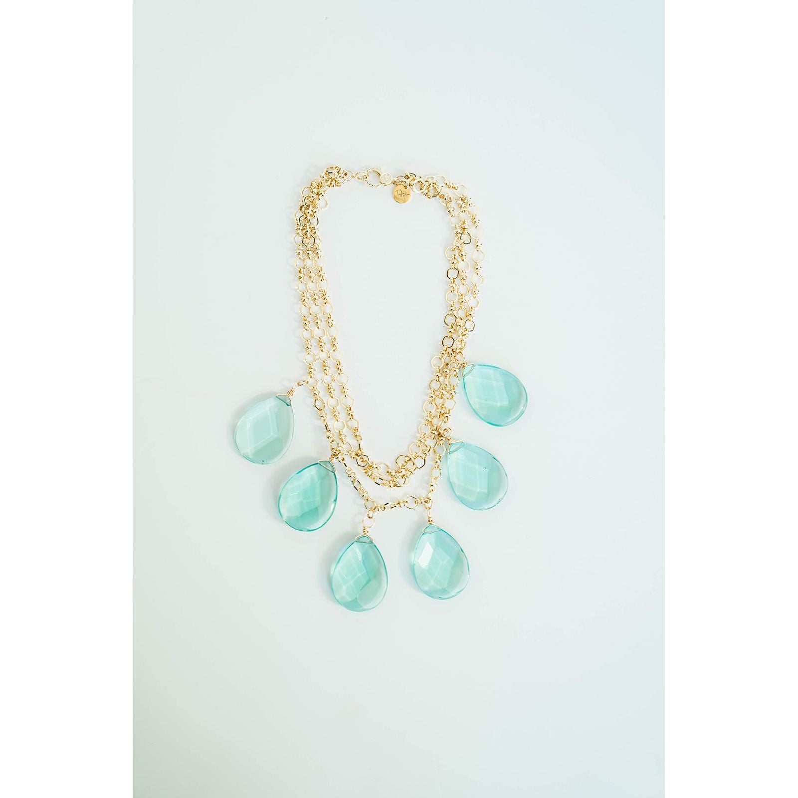Gold layered chain necklace with turquoise teardrop pendants on a light grey background
