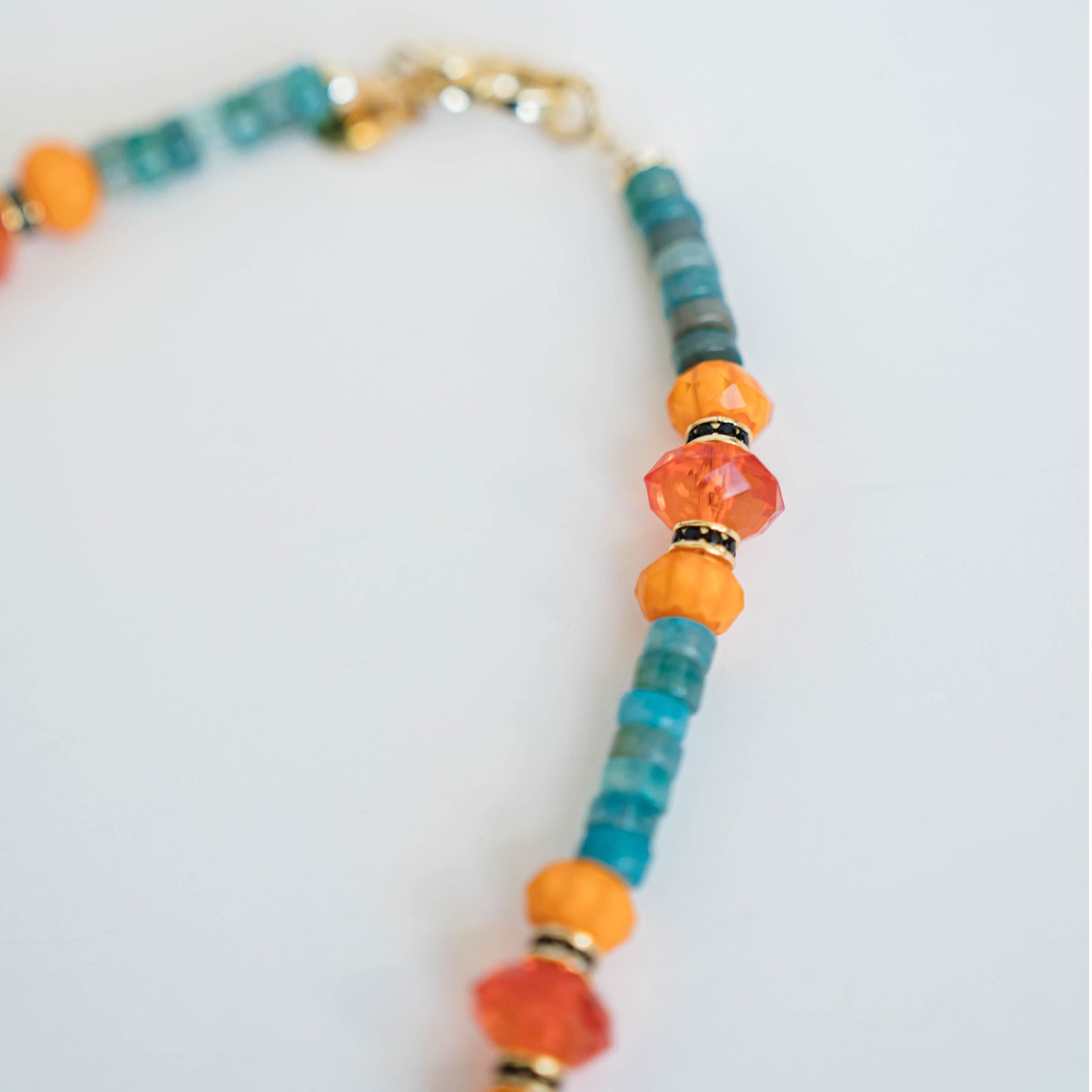 necklace with blue, turquoise, orange beads and black and gold pave spacers on a light background