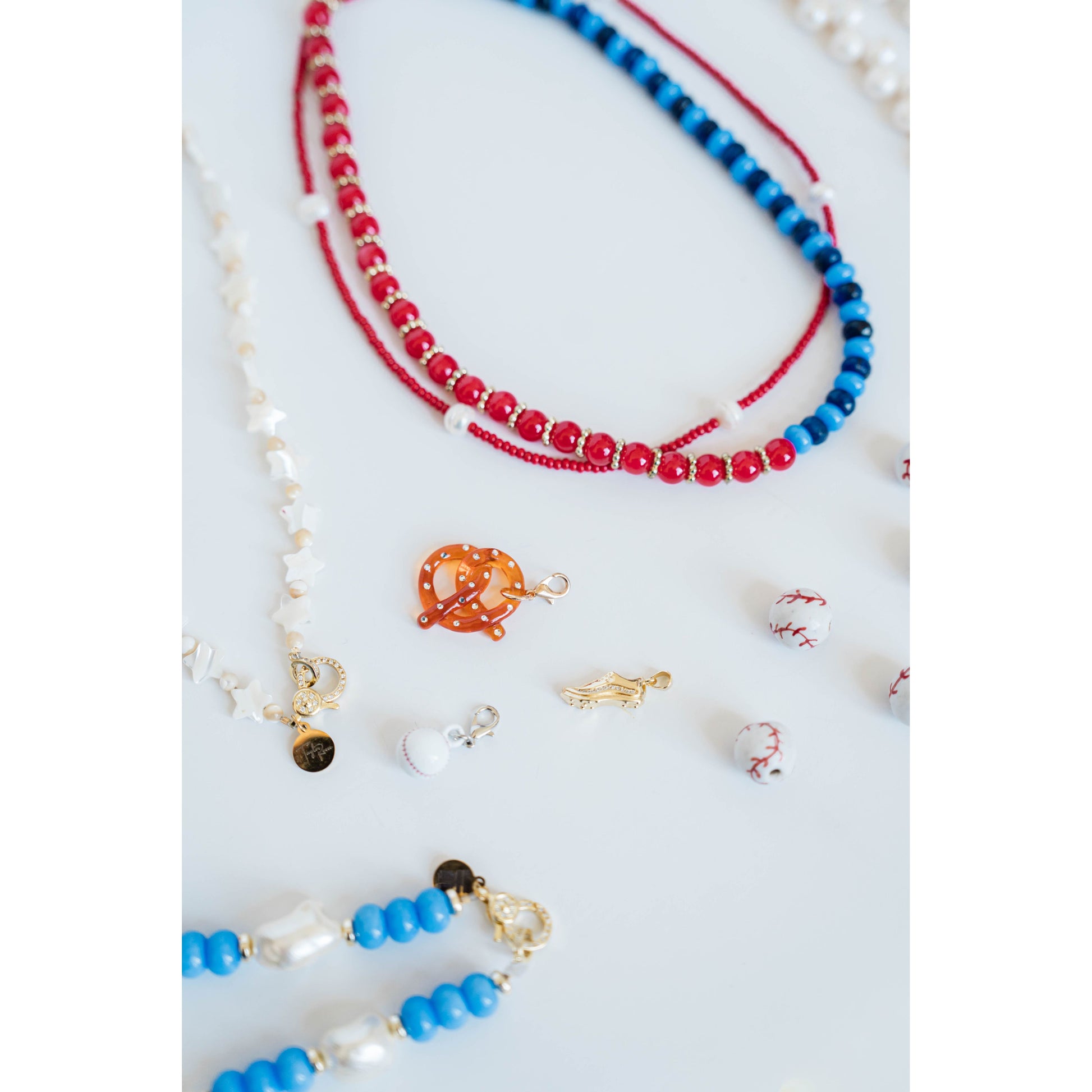 Close-up of various baseball-themed red white and blue necklaces and with baseball beads and baseball game charms on a white background