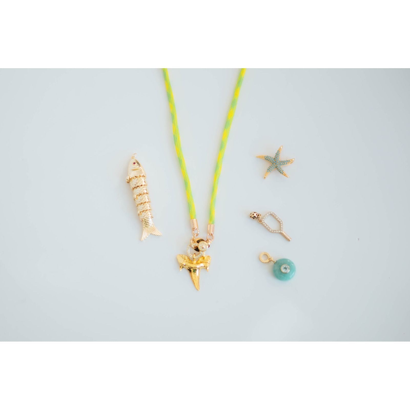 neon cord necklace with collection of gold starfish, fish, and shark tooth charms on a light grey background