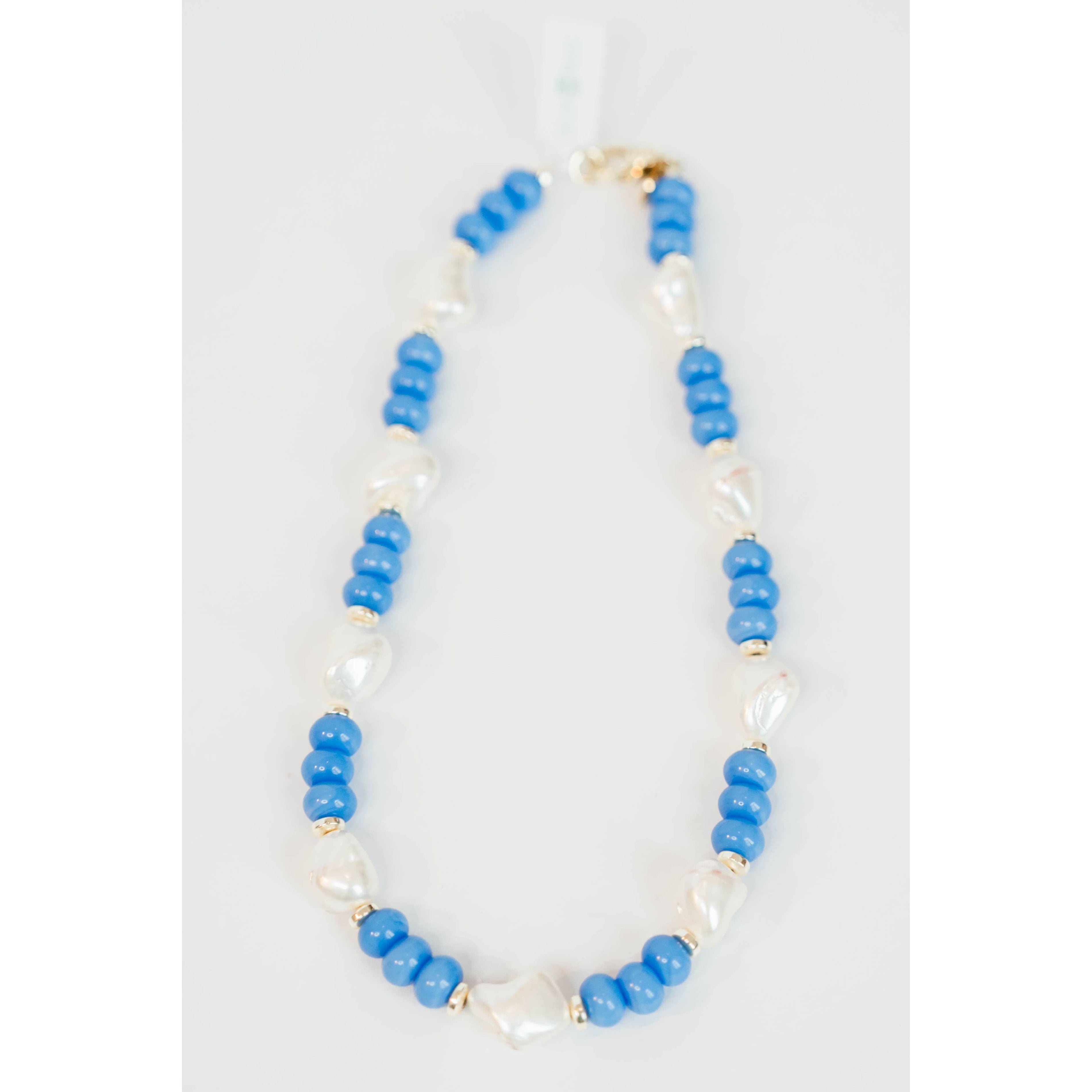 chunky beaded necklace with blue round beads and gold spacers and large pearl beads with a gold pave clasp on a light grey background