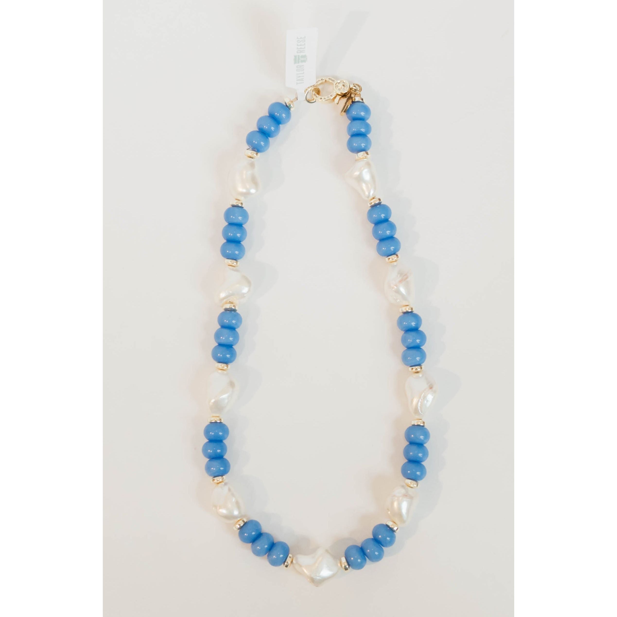 chunky beaded necklace with blue round beads and gold spacers and large pearl beads with a gold pave clasp on a light grey background