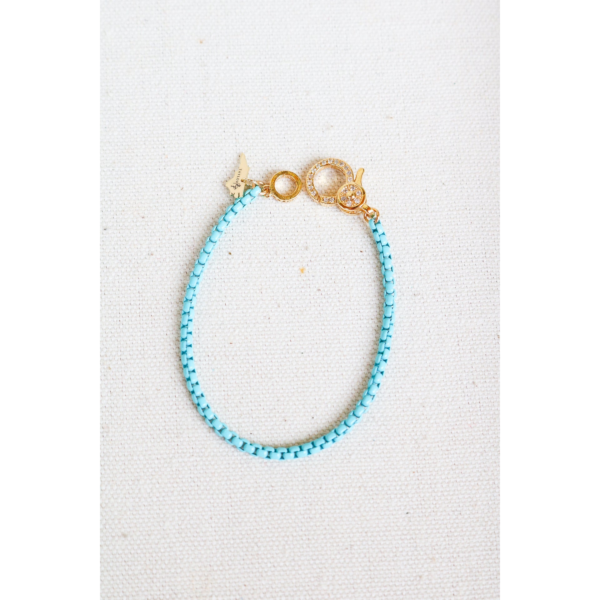 light blue box chain bracelet with a gold pave lever clasp on a light grey background