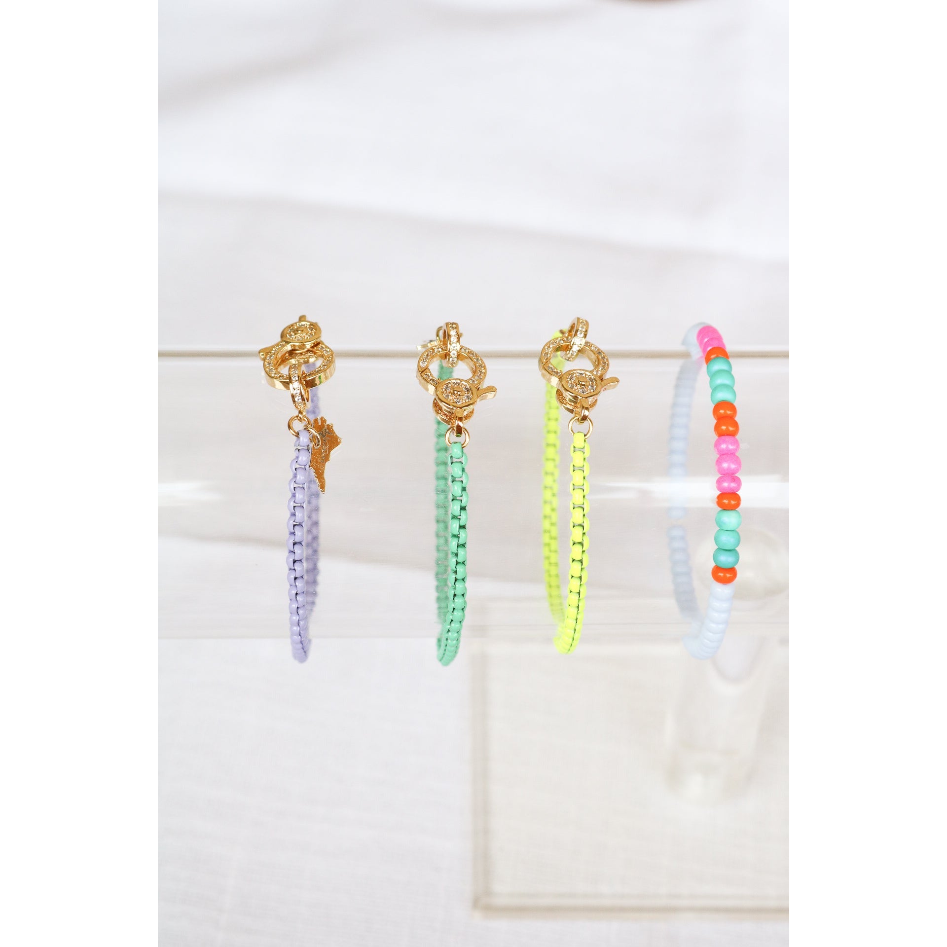 3 enamel chain bracelets in lavender, mint green, and yellow with gold pave lever clasps on a clear bracelet holder
