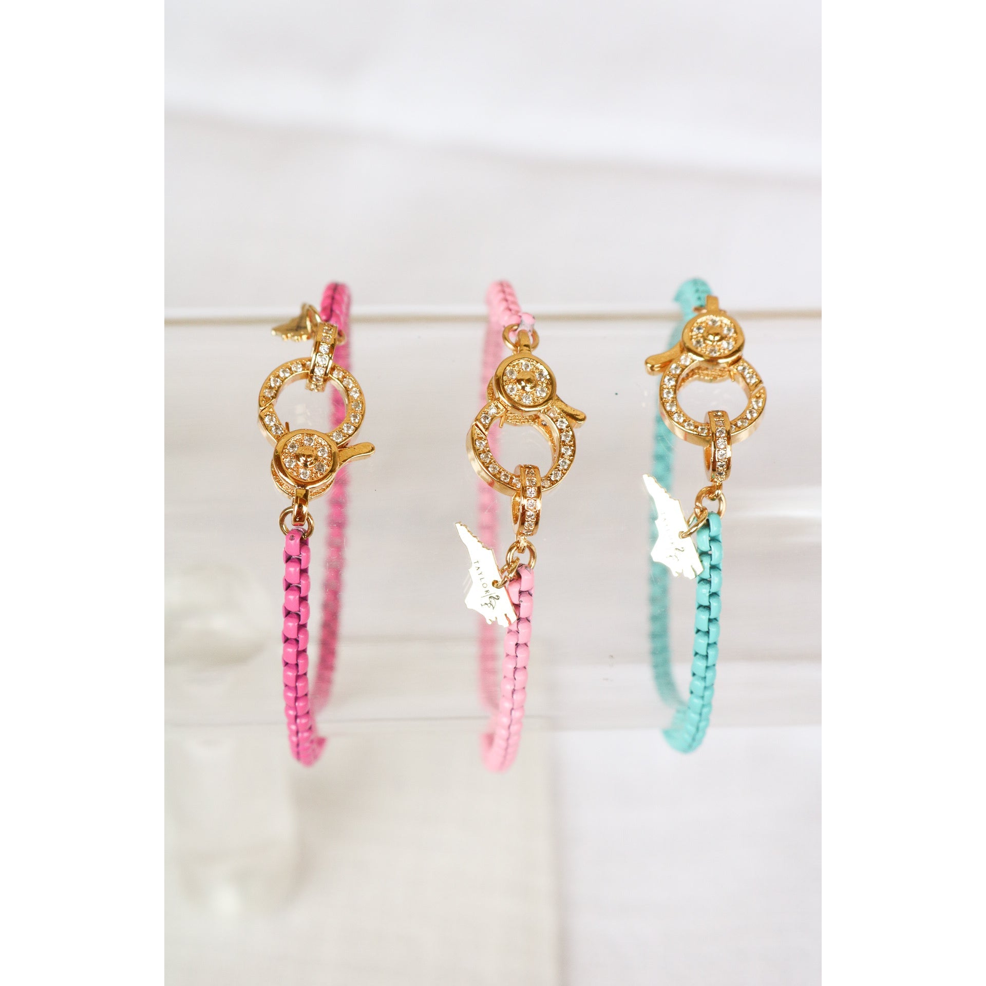 set of 3 colorful chain bracelets in hot pink, light pink, and teal blue with gold pave lever clasps on a clear bracelet holder