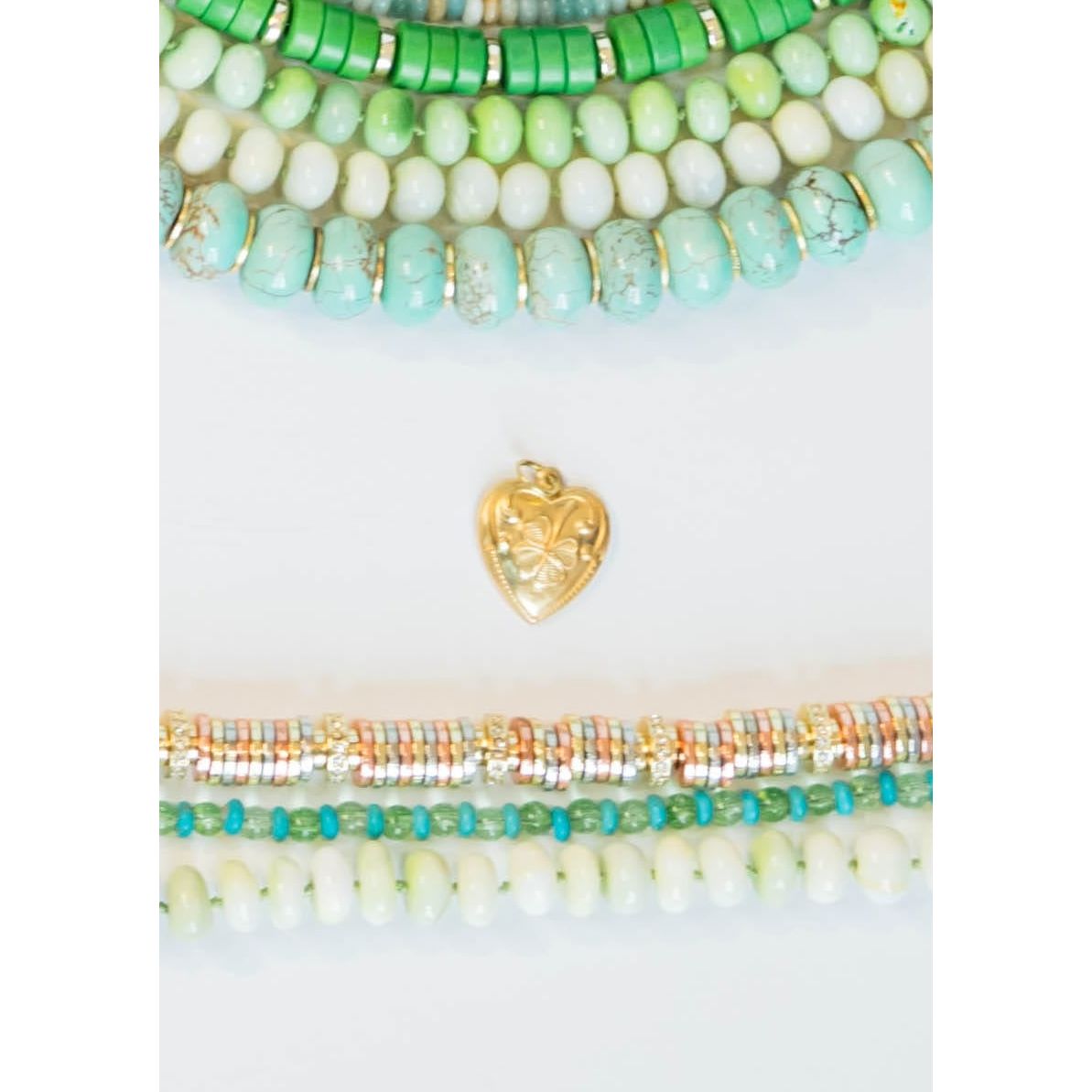 Set of colorful green and gold beaded necklaces with a gold heart clover charm on a white background
