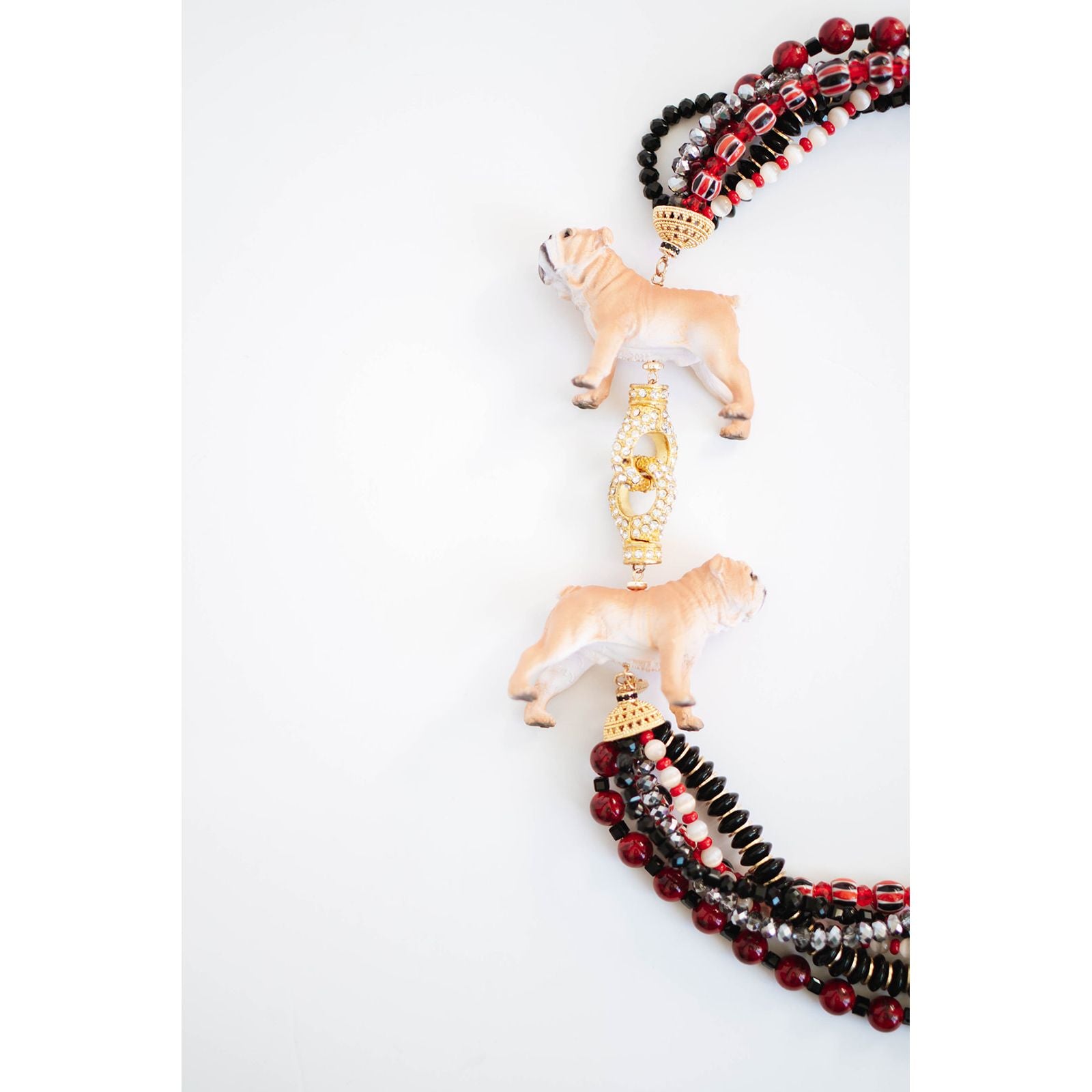 statement necklace with layered strands of red, black, and gold beads and two dog pendants with a gold pave clasp on a white background