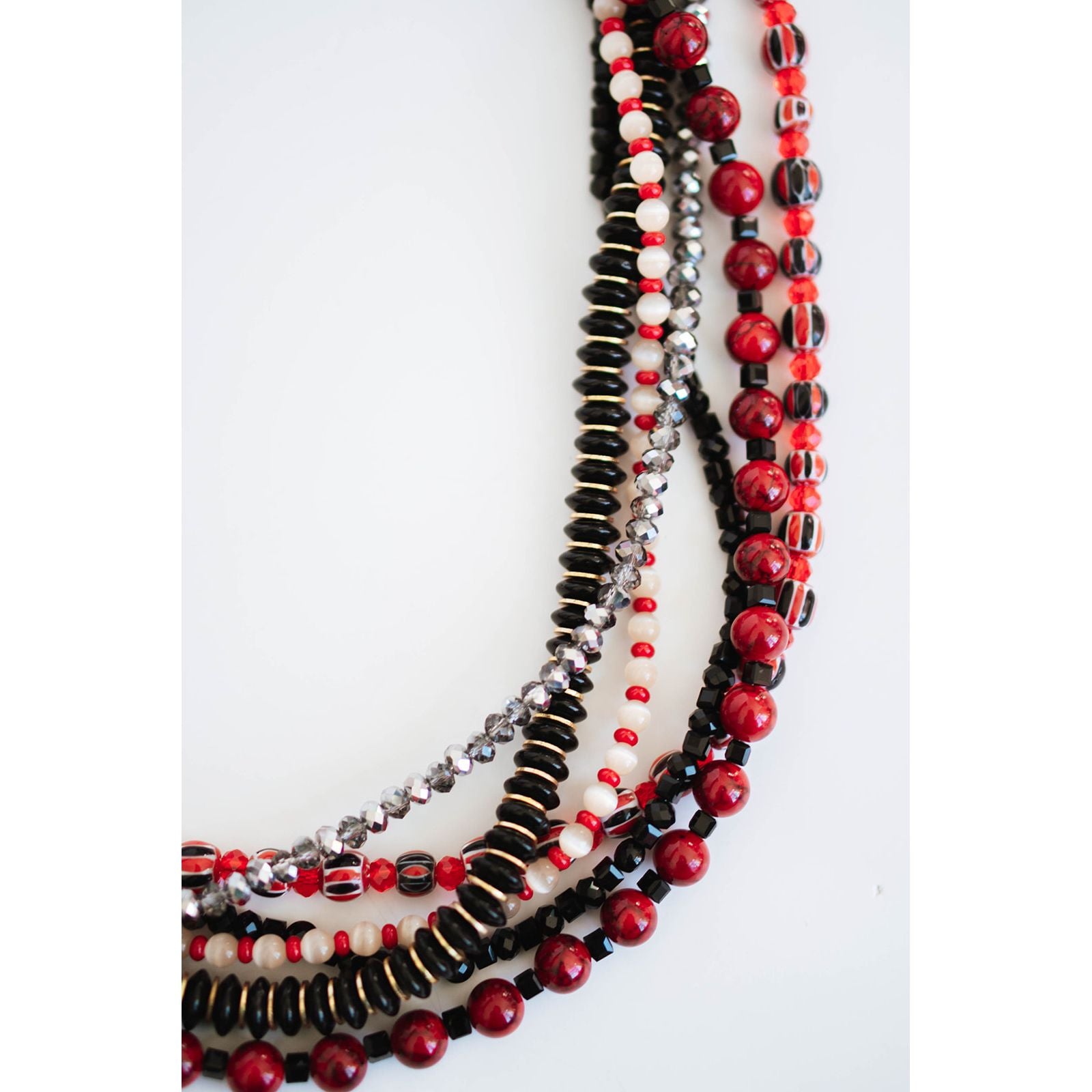 stack of various red, black, and gold beaded necklaces on a light background