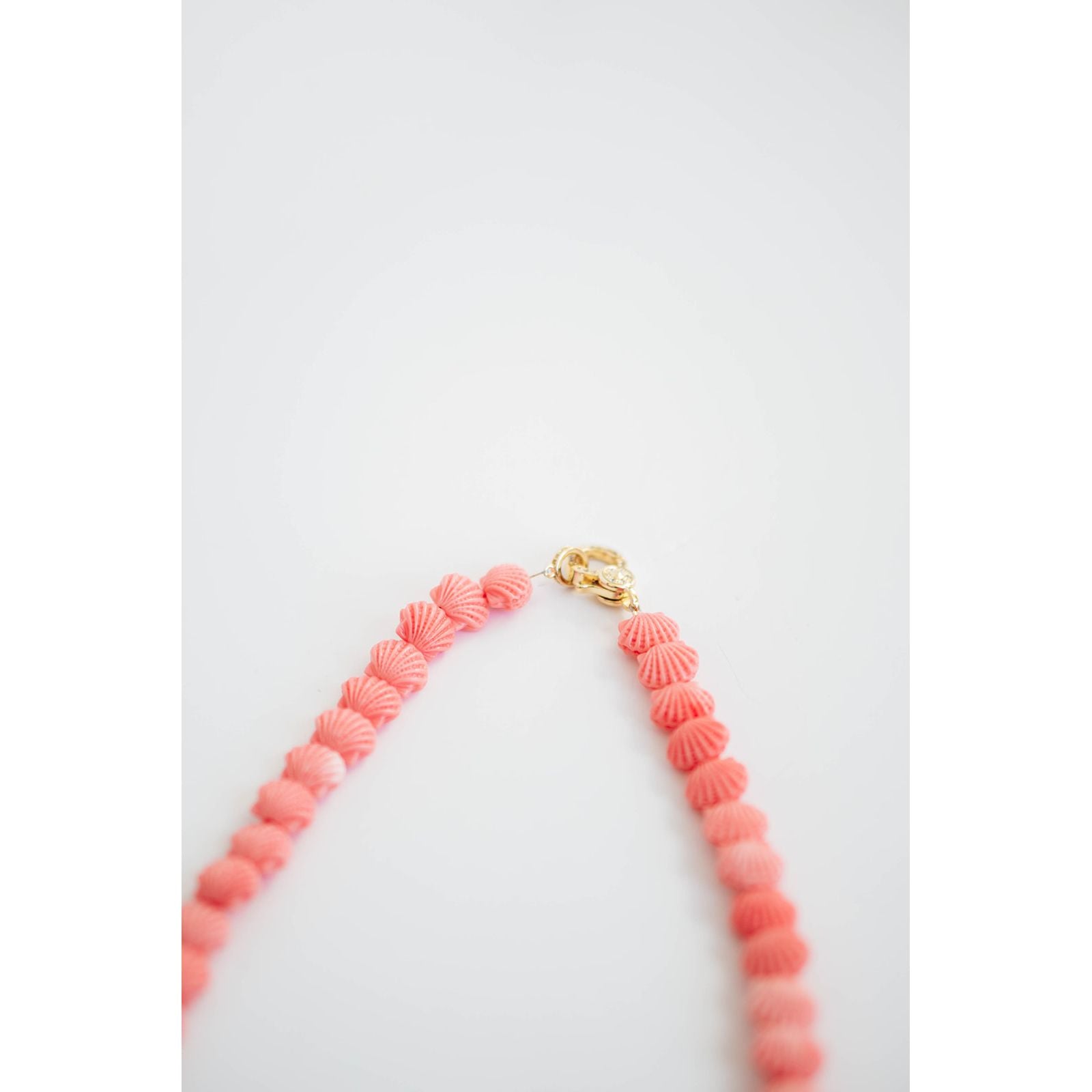 Necklace with pink shell-like beads with gold pave clasp on a light gray background