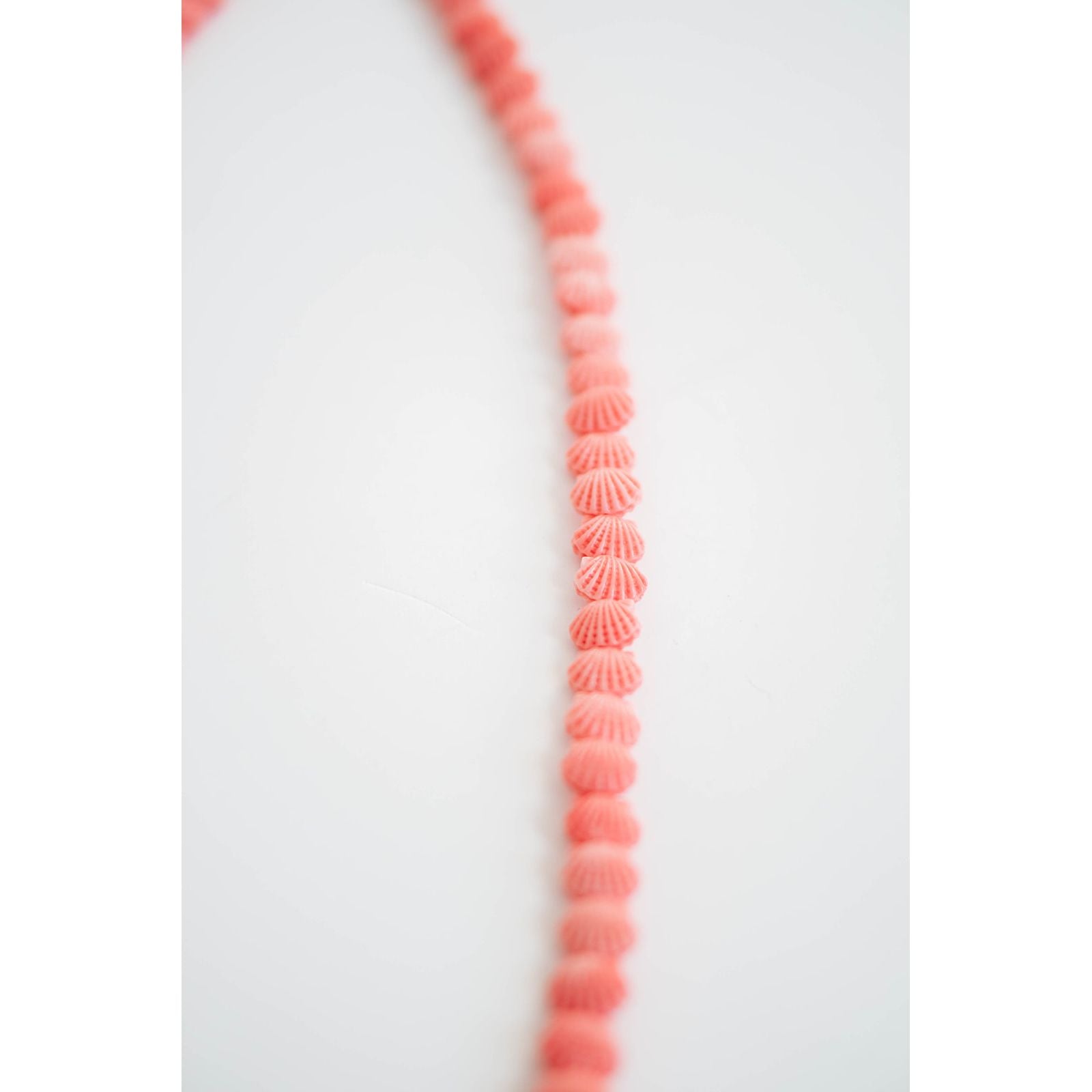 Necklace with coral pink shell-like beads on a white background