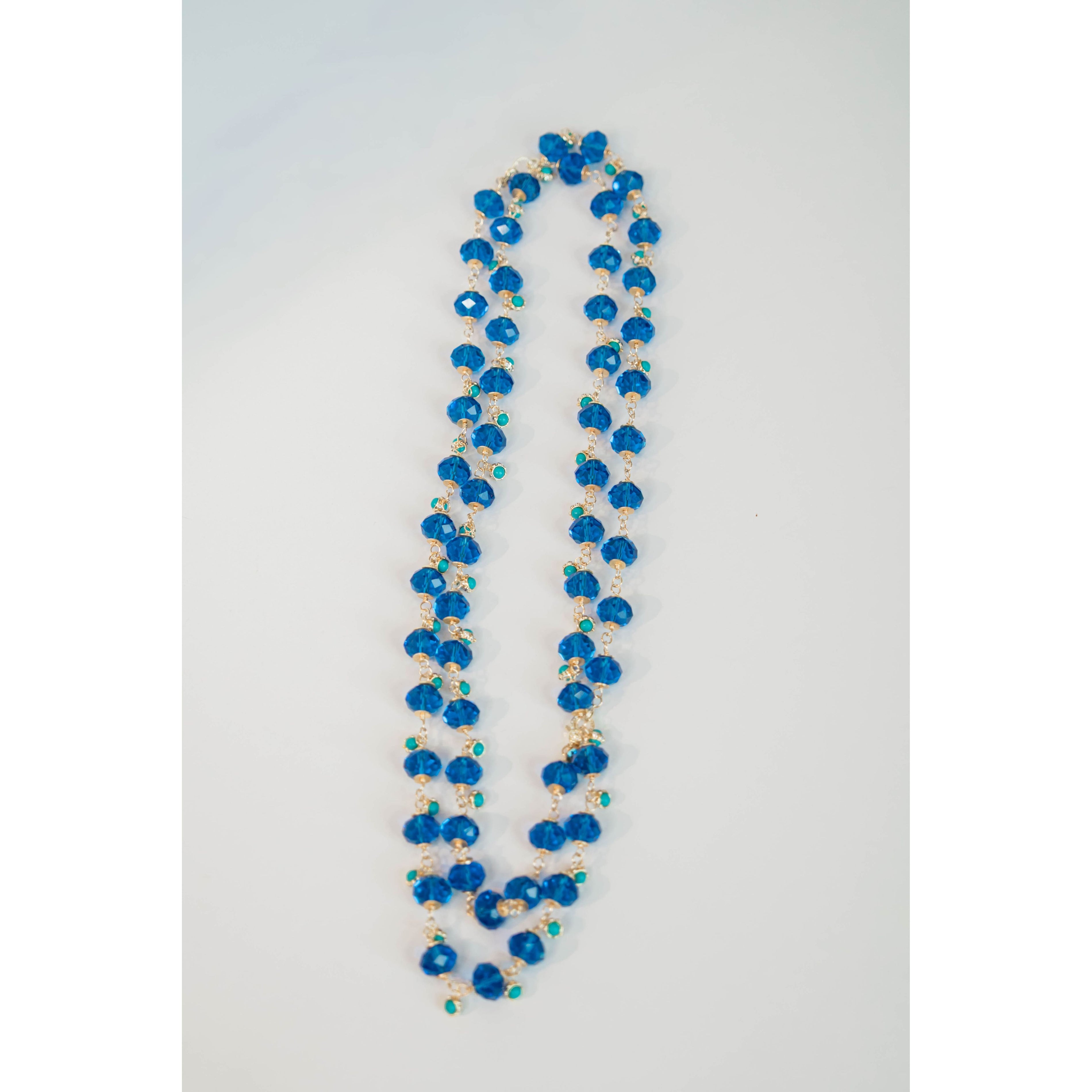 Long beaded necklace with crystal blue and turquoise and gold chain on a light gray background