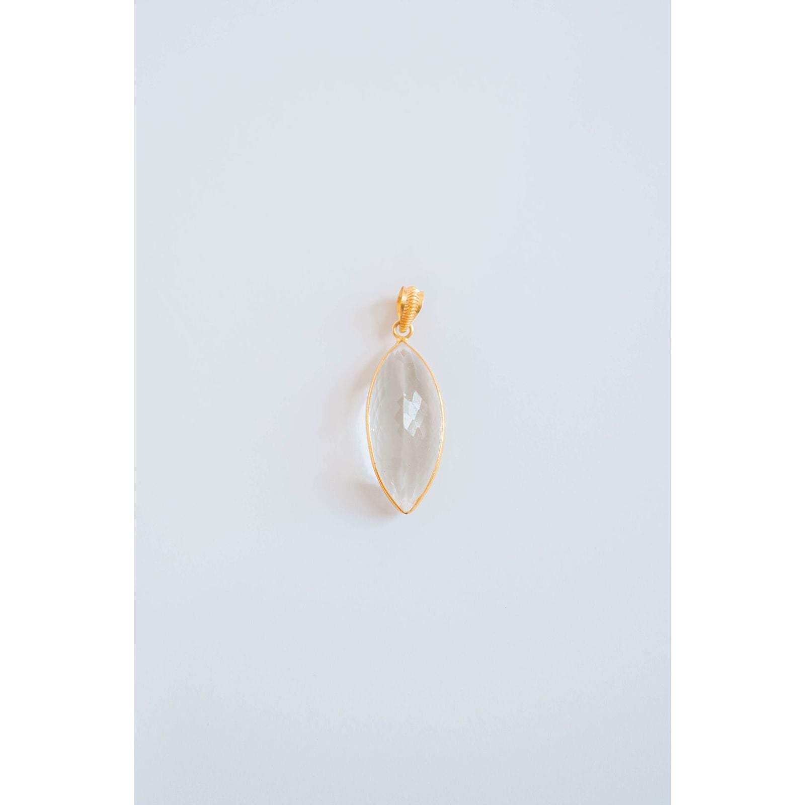 oval shaped gold pendant with a clear stone on a light gray background