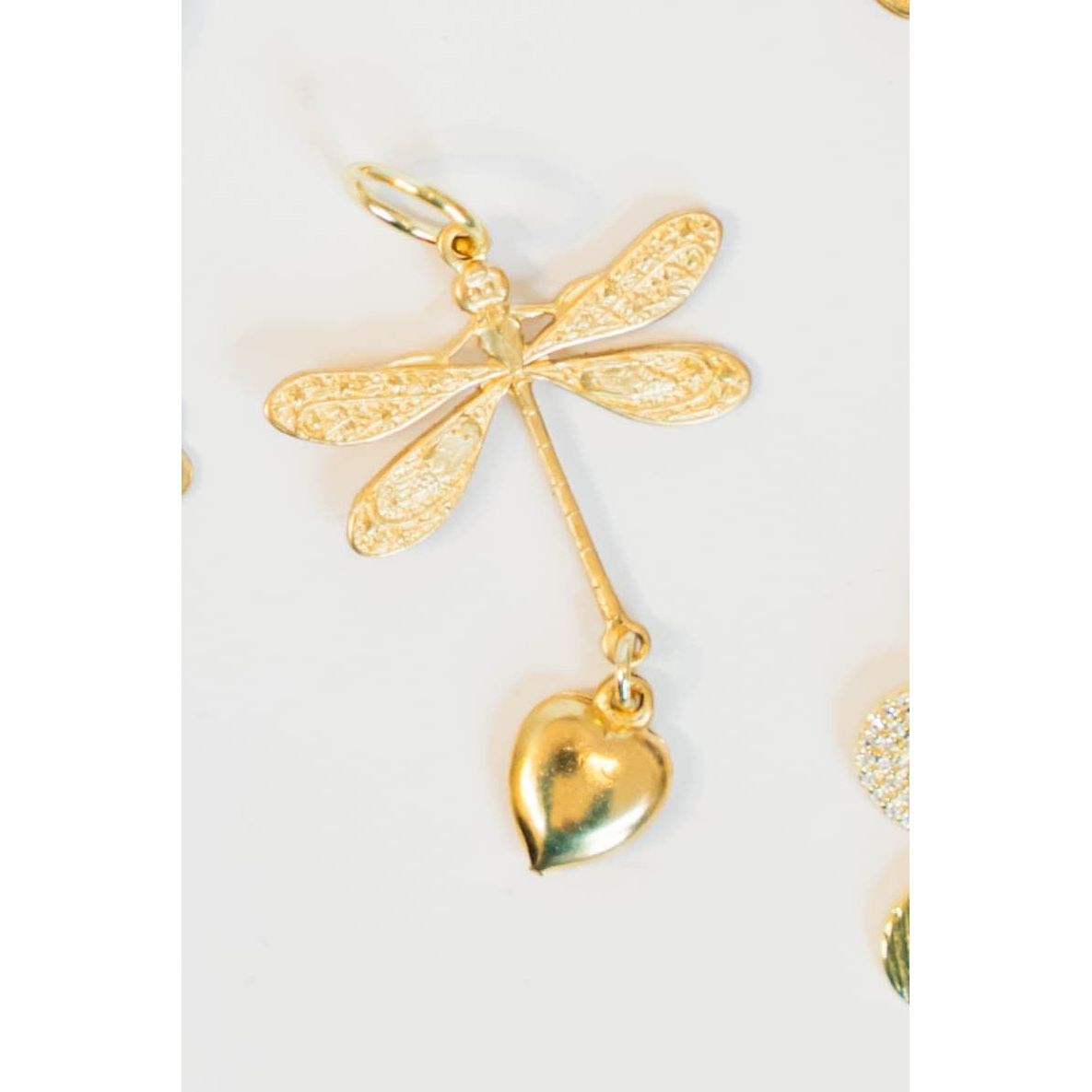 Gold dragonfly pendant with a heart charm on a white background