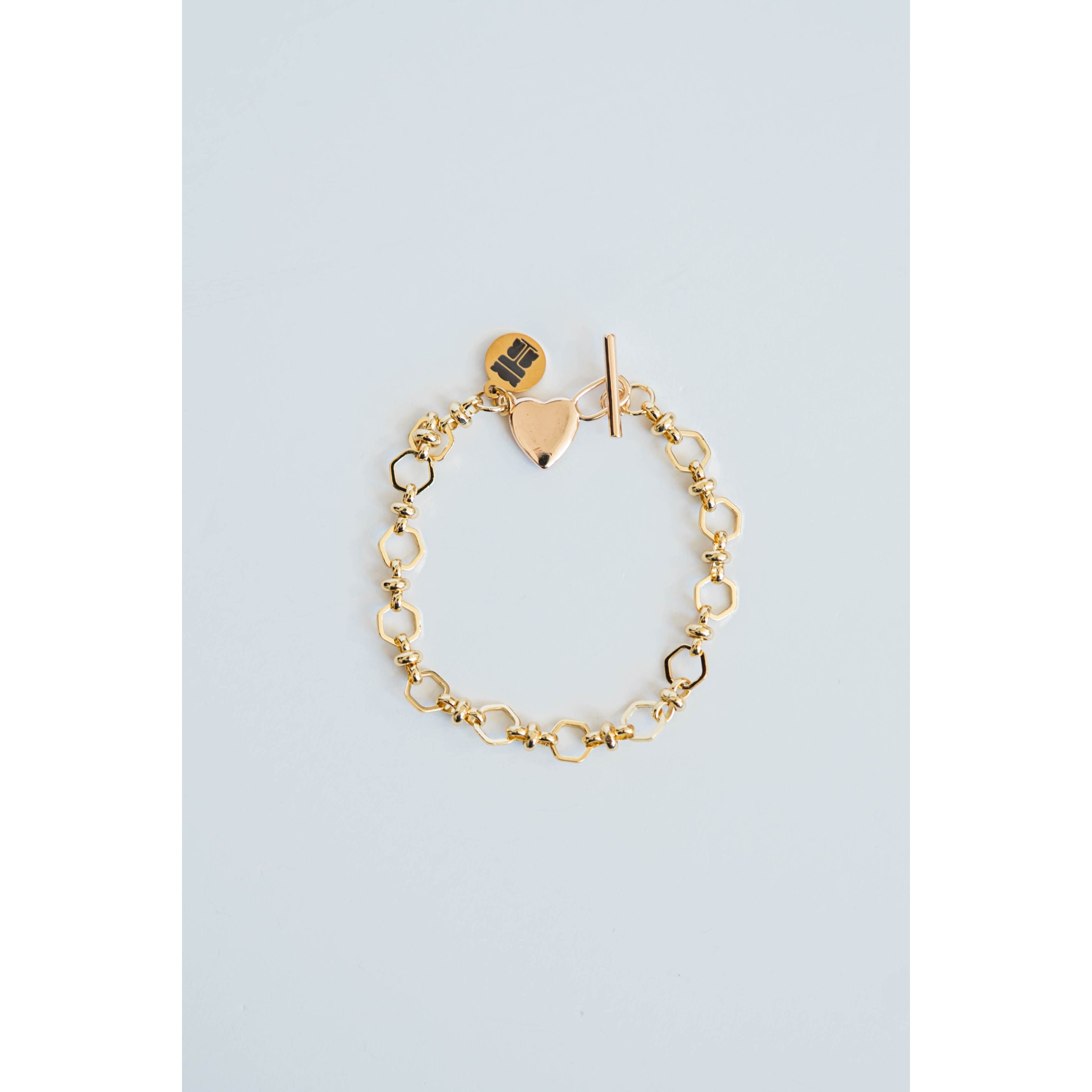 Gold chain bracelet with heart-shaped charm and toggle clasp on a light blue background