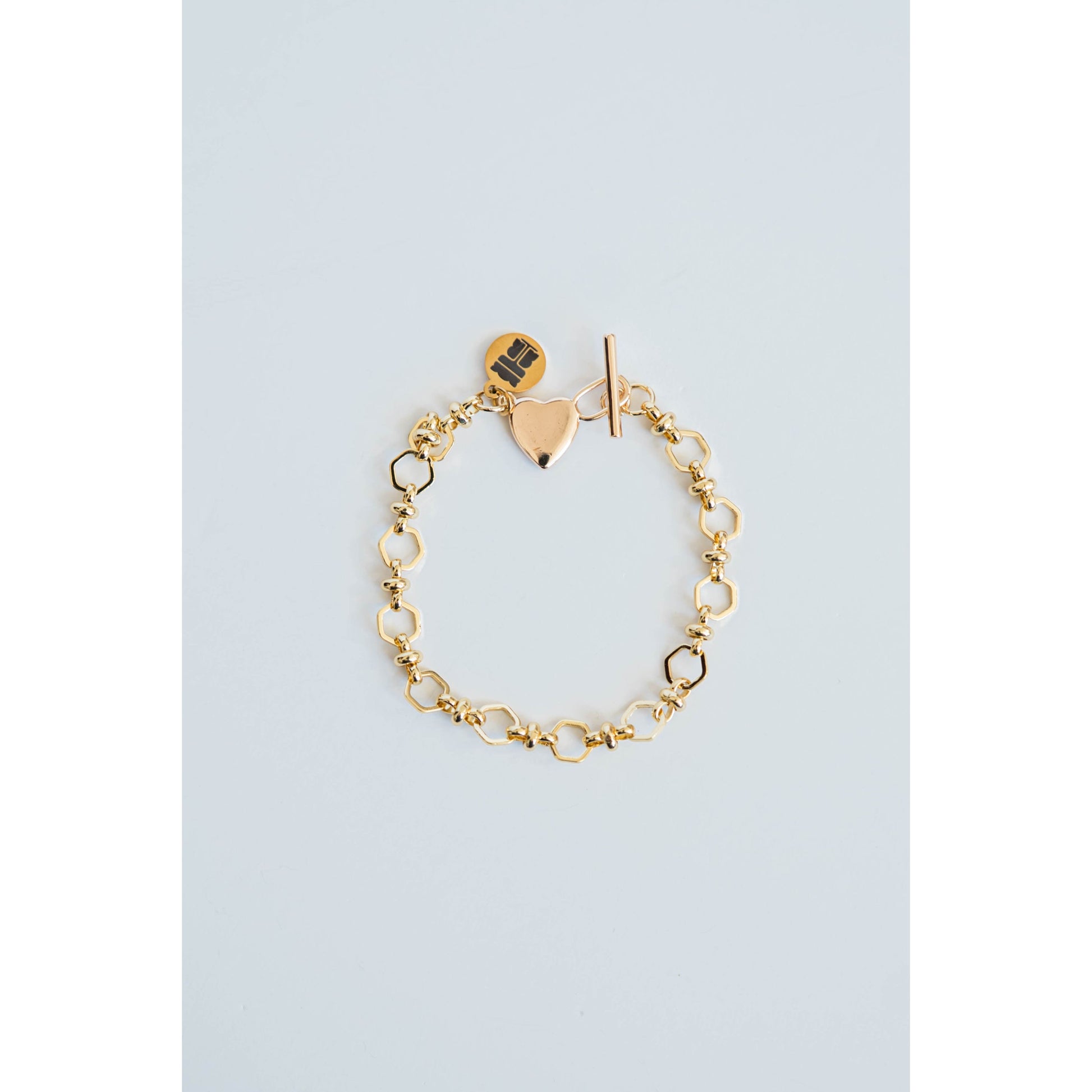 Gold chain bracelet with heart-shaped charm and toggle clasp on a light blue background