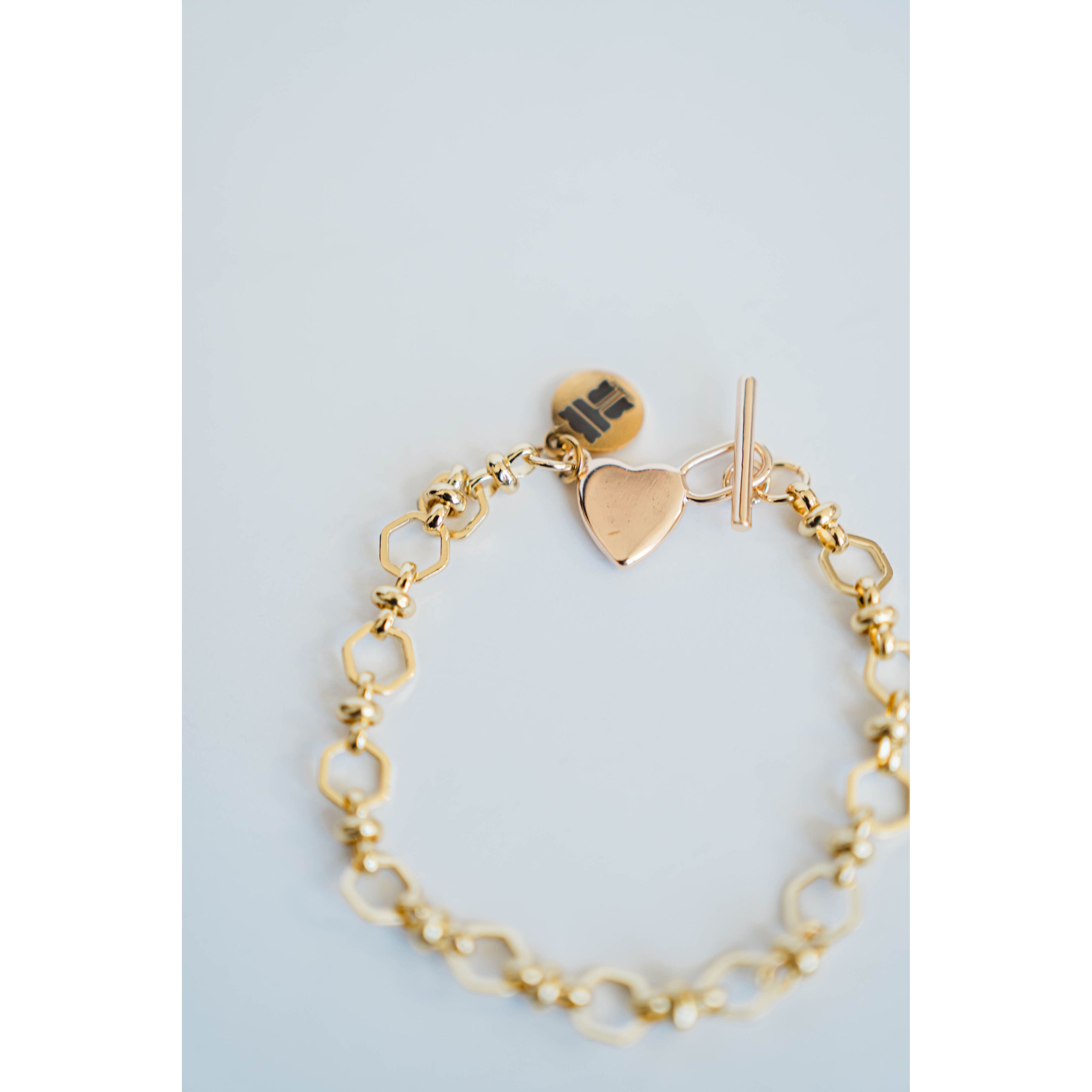 Gold bracelet with heart charm and toggle clasp on a light blue background