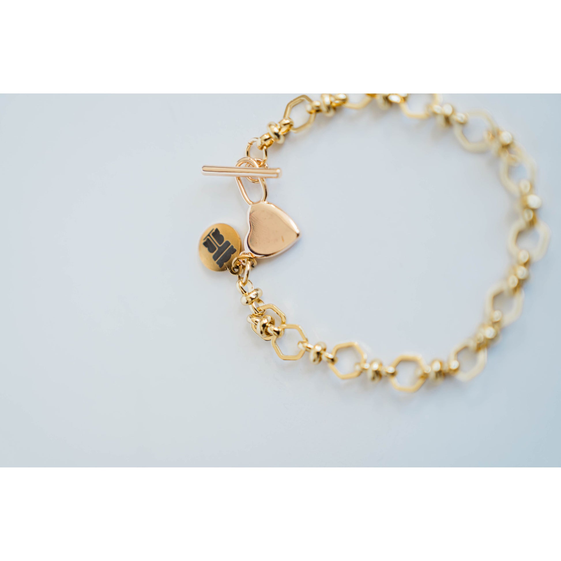Gold chain bracelet with heart charm and toggle clasp on a light gray background