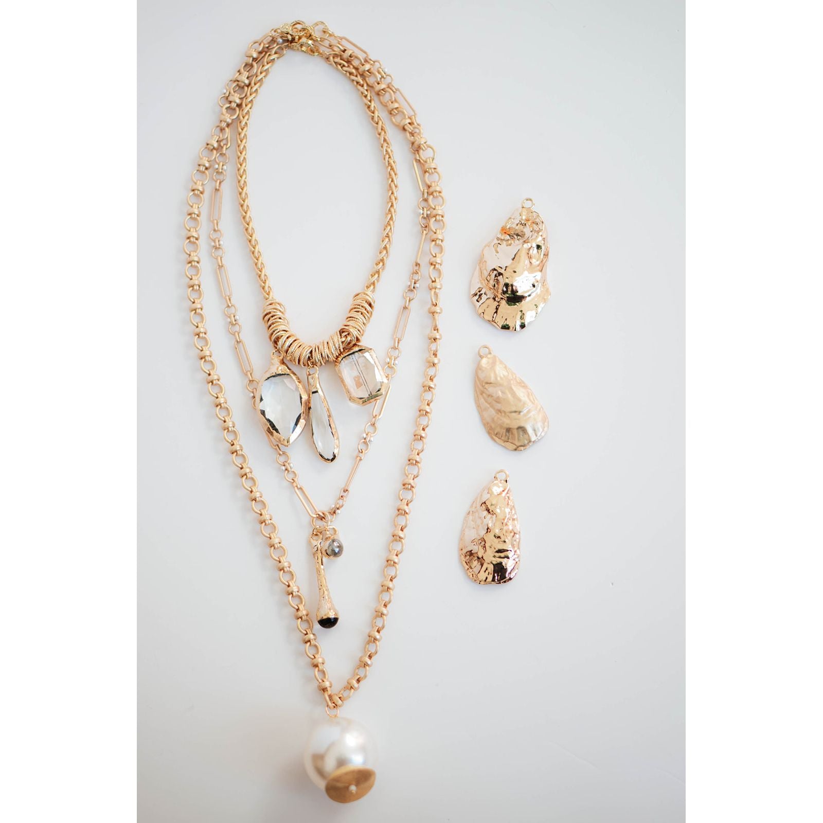 set of three gold layered necklaces with pearl pendants and gold oyster shell pendants on a light background