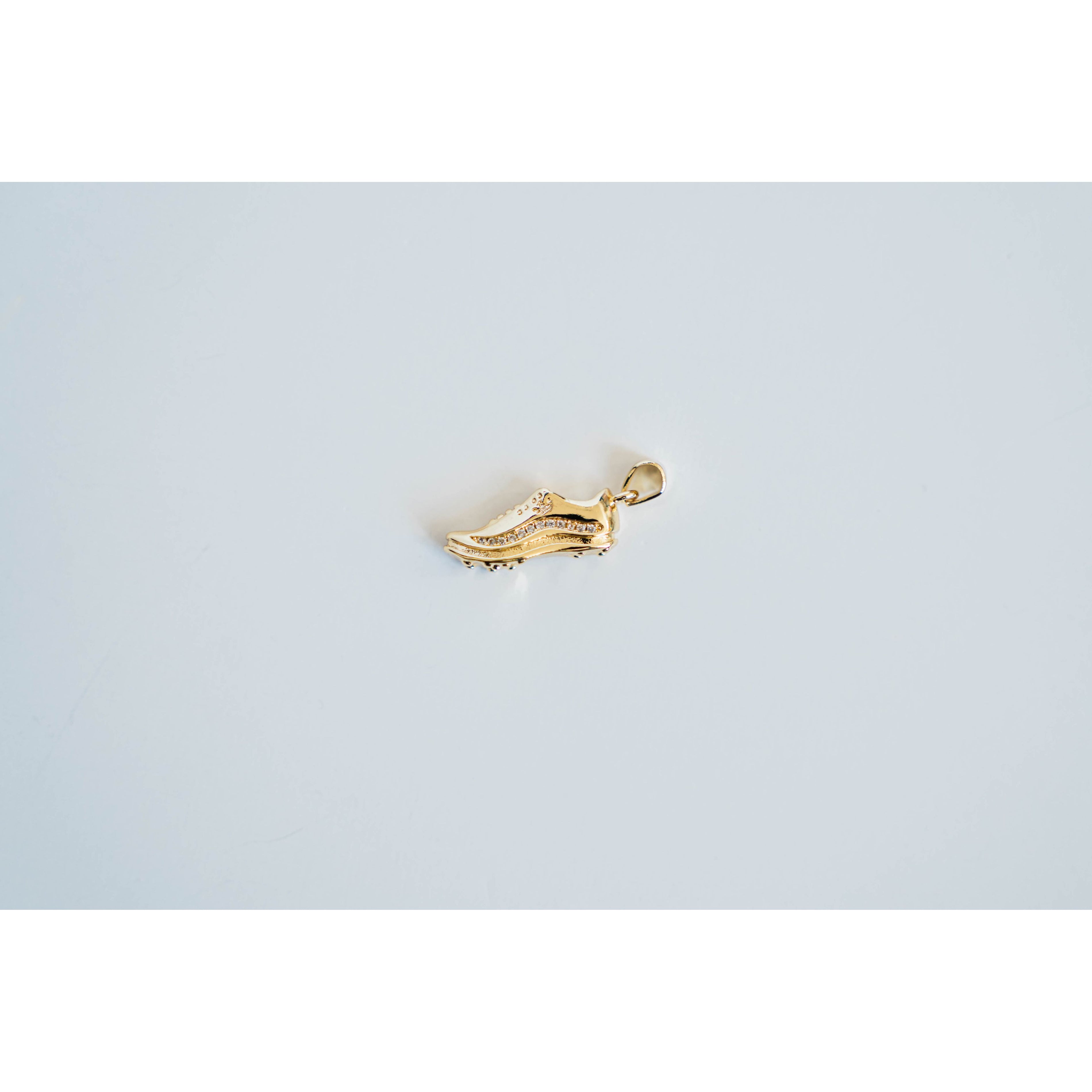 Gold shoe-shaped charm with pave detailing on a light gray background