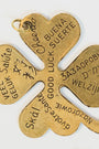 gold/brass four leaf clover charm with "good luck" engraved in different languages on a light background