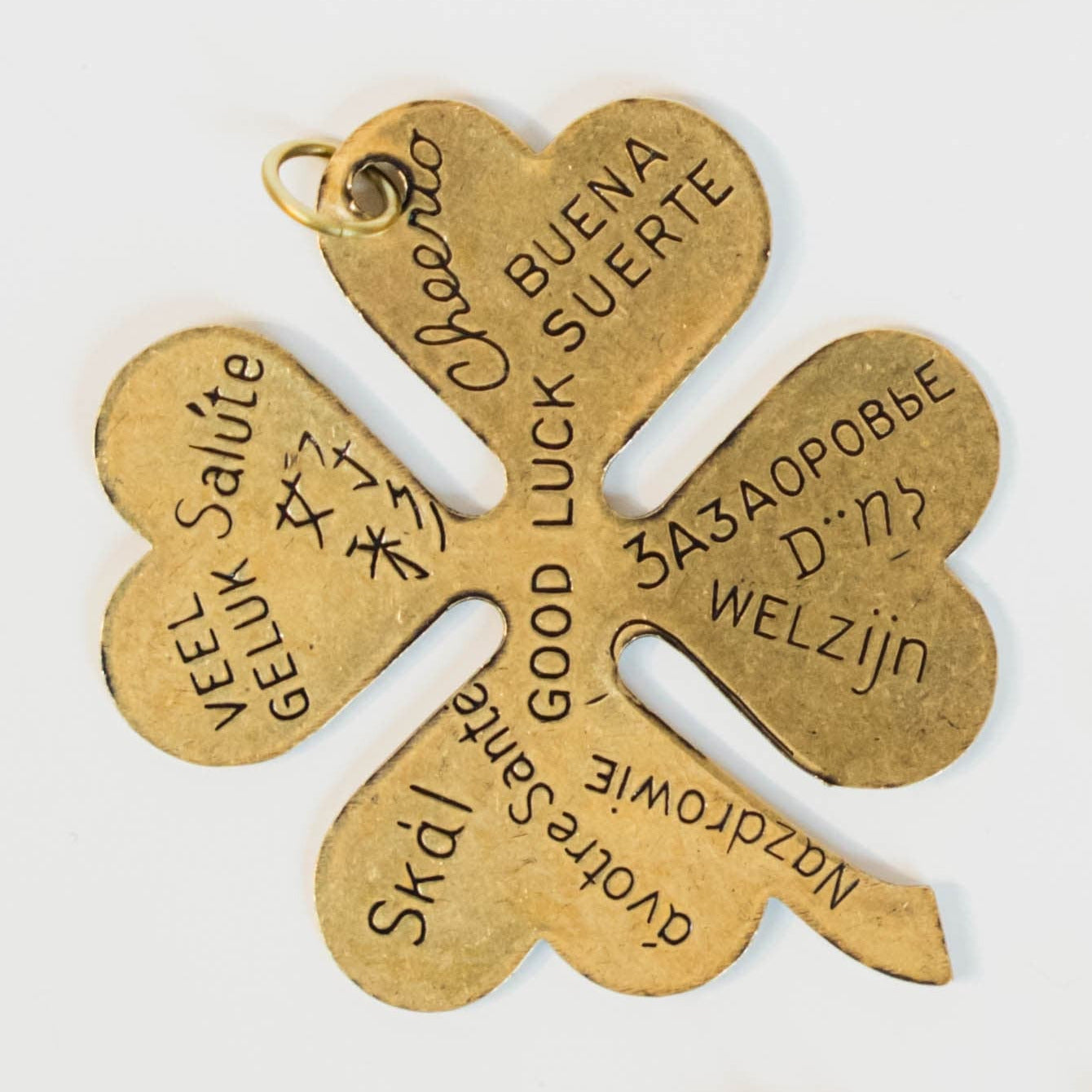 gold/brass four leaf clover charm with "good luck" engraved in different languages on a light background