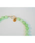 closeup shot of a light green beaded necklace with a gold pave lever clasp against a light background