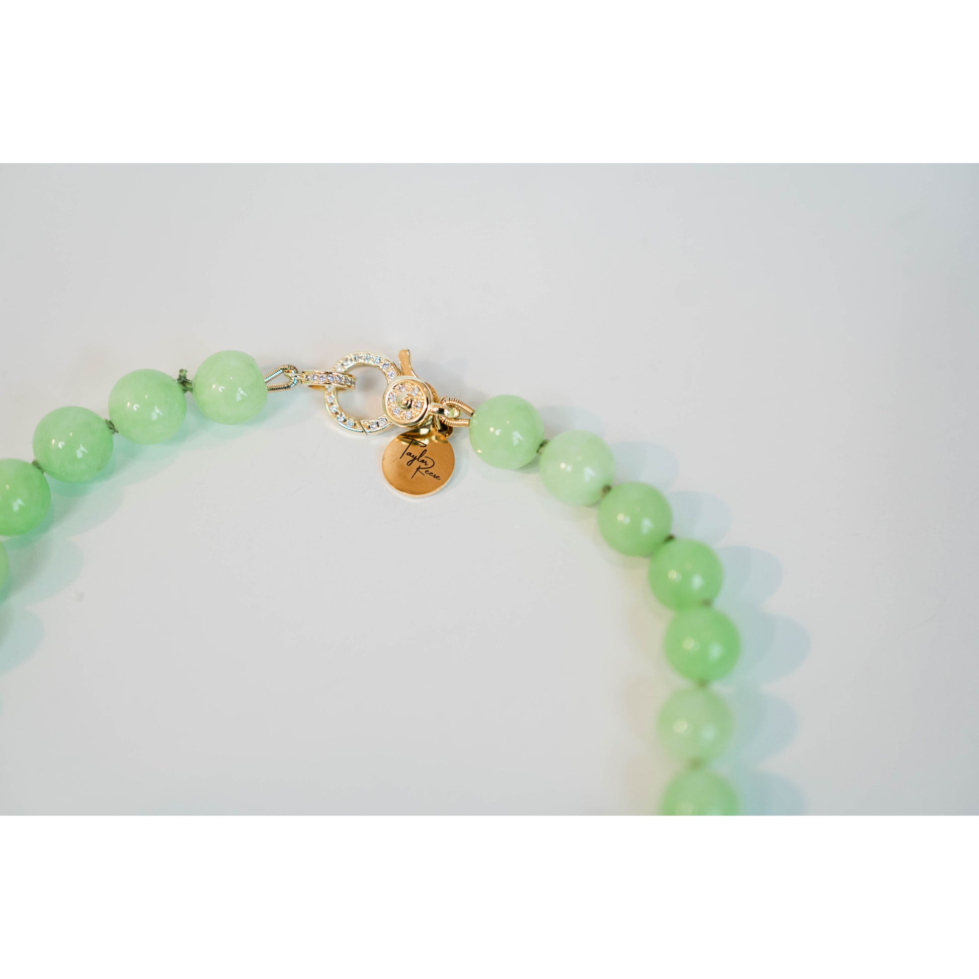 closeup shot of a light green beaded necklace with a gold pave lever clasp against a light background