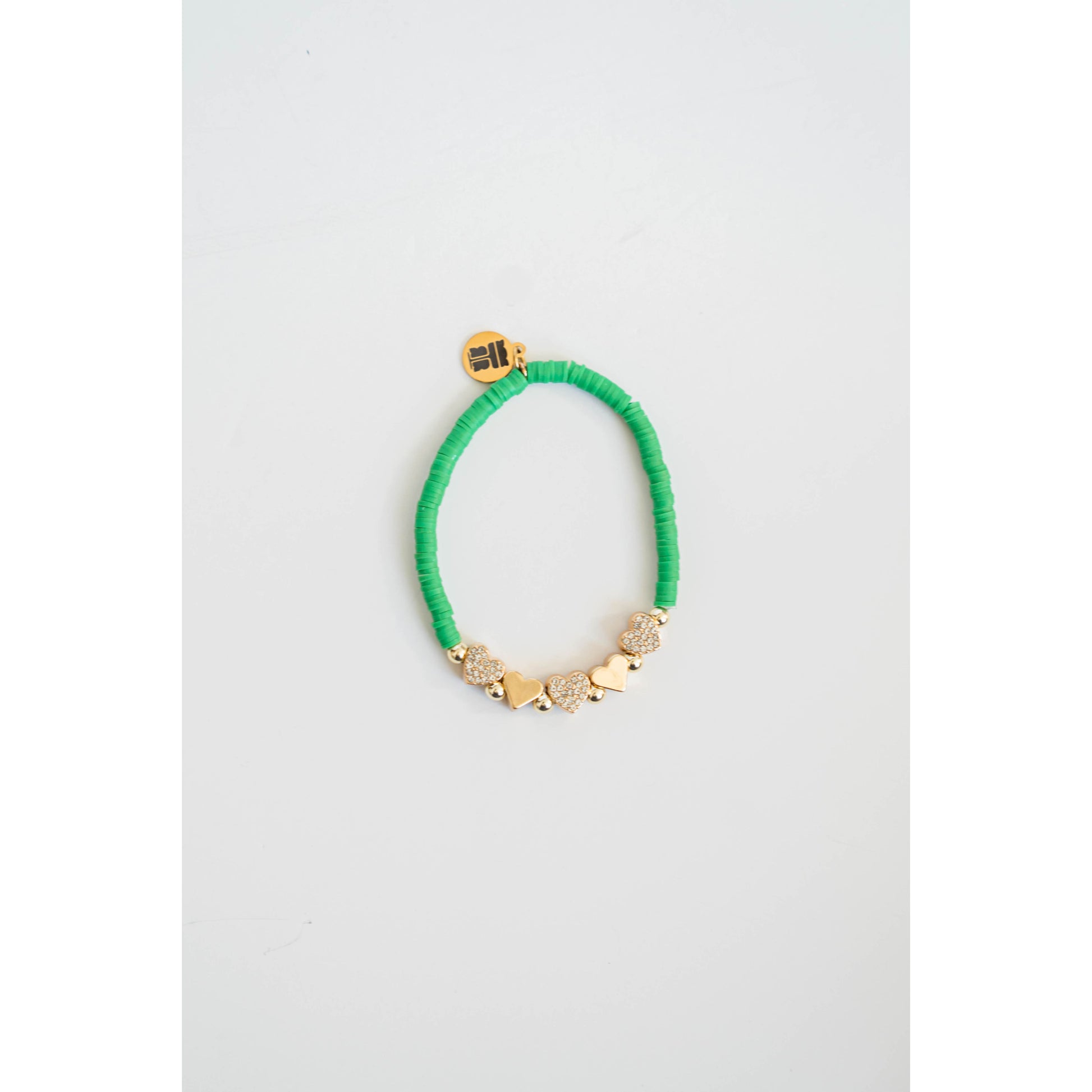 Green beaded bracelet with gold pave heart accents on a light gray background