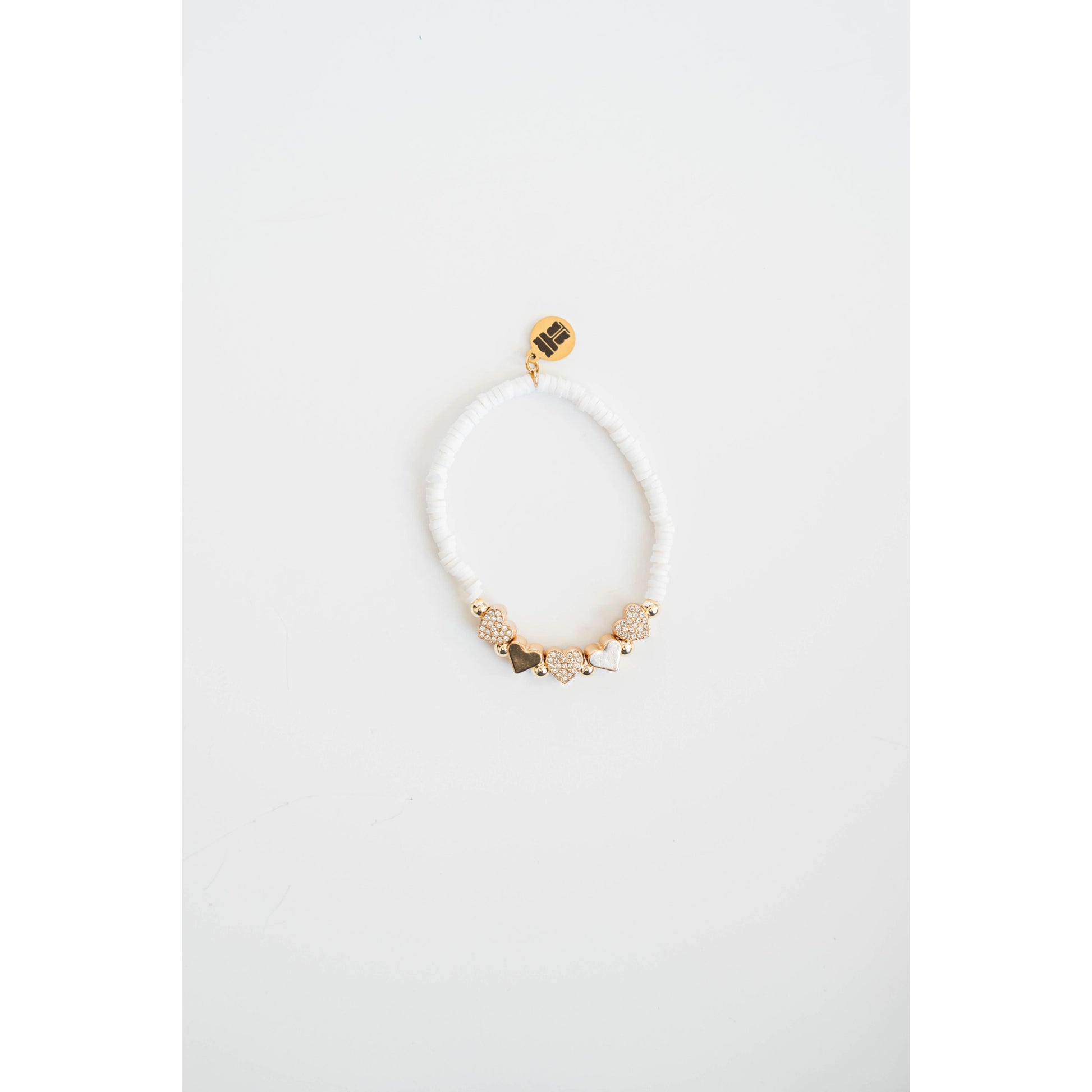 white beaded bracelet with gold pave heart shaped beads on a light gray background