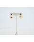 Gold heart-shaped earrings with an emerald green stone stud on a white stand against a light gray background
